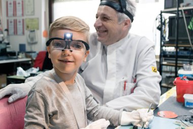 Smiling kid with magnifying eyeglasses repairing circuit board with his science teacher in tech laboratory.