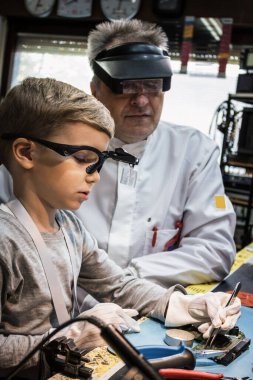 Small science student repairing mother board while being in engineering laboratory with his teacher.