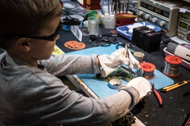Small kid examining mother board in tech laboratory. Kid repairing computer part for school science project in IT lab. 