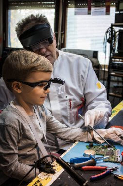 IT technician showing to small boy malfunction on a circuit board while working on school science project in tech laboratory.