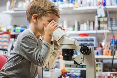 Small science student examining something while looking through microscope in IT laboratory.