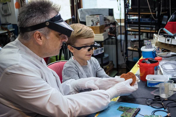 Male teacher teaching small boy how to repair computer part in laboratory during school science project.