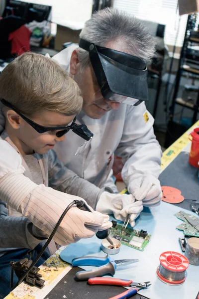 Science teacher and small boy soldering mother board in a labora