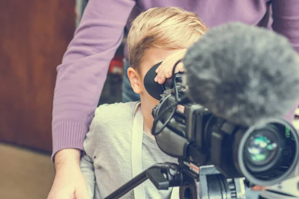 Small kid filming with video camera with help of movie director in a studio.
