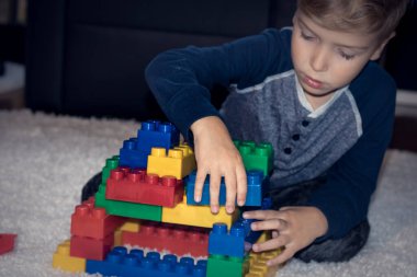 Creative kid making something with toy blocks. Small boy playing with plastic blocks at home.
