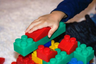 Close up of child playing with plastic blocks. Creative kid building something with toy blocks on the carpet.
