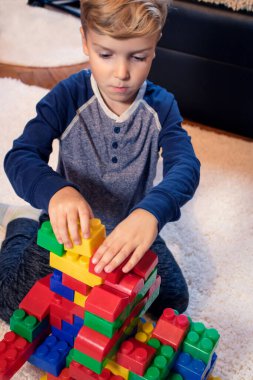 Creative child building with toy blocks on the carpet. Little boy playing with plastic blocks on the floor.