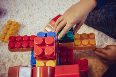 Close up of child playing with plastic blocks. Creative kid building something with toy blocks on the carpet.