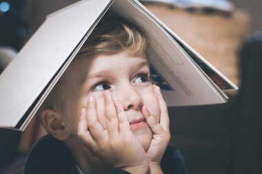 Close up of small boy holding book on his head. 