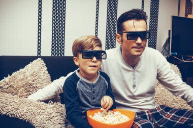 Father and son eating popcorn while watching 3d movie and relaxing at home.