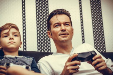 Smiling father playing video games with his son at home.