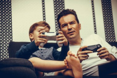 Little boy and his father playing online video games at home. 