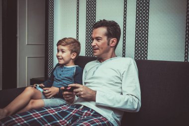 Happy kid and his father having fun while playing video game in the living room.