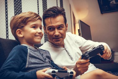 Happy boy and his father having fun while playing video games together.