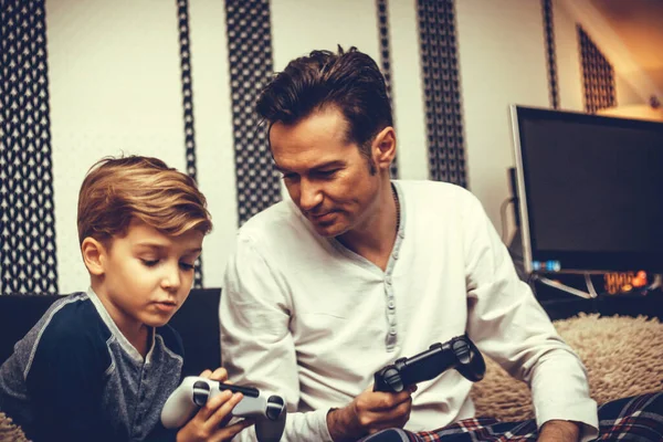 Small boy playing video game with his father and teaching him how to use game controller. 