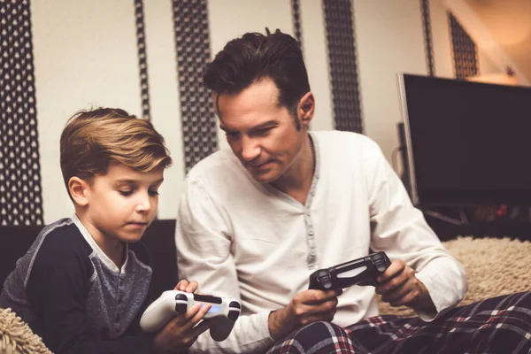Little boy showing his dad how to play game and use game controller while spending time together at home.