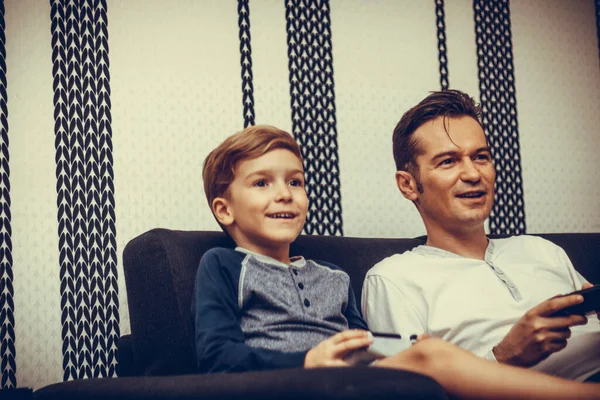 Happy kid and his father playing video games and having fun together at home.