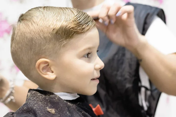 Close-up of cute kid having haircut at hair salon. 