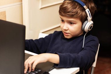 Cute kid with headphones using laptop and playing video games at home. 