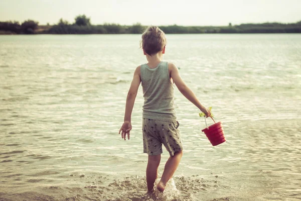 Rear view of kid with beach toys walking in the sea on summer vacation. 