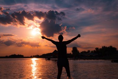 Silhouette of carefree woman with arms outstretched enjoying in freedom and summer at sunset. 