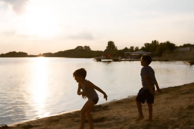 Playful boys having fun on the beach at sunset during summer day.