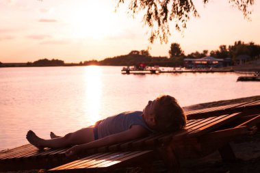 Little boy on deck chair relaxing at beach and enjoying in summer holiday at sunset. 