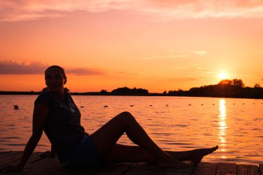 Relaxed woman enjoying the sunset while sitting on a pier by the sea on summer vacation. 