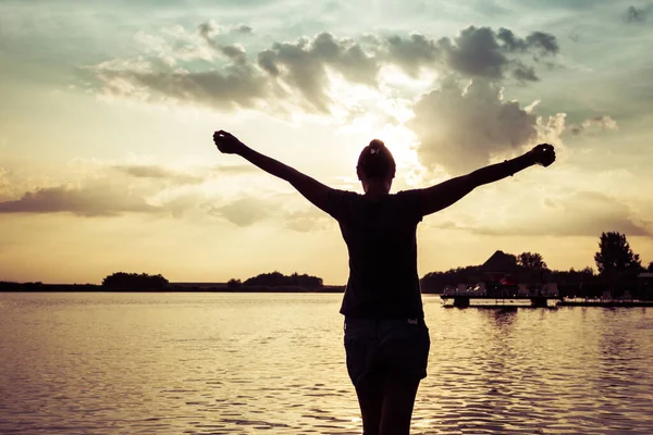 Rear view of woman with arms outstretched having fun on the beach at sunset.