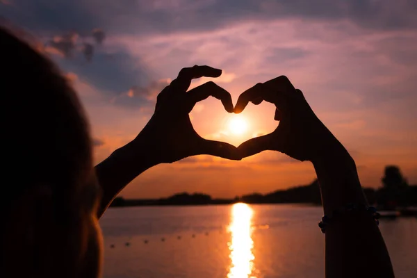 Sun in heart shaped hands. Silhouette of woman making heart shape at sea sunset.