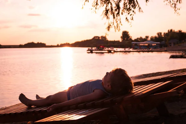 Little boy on deck chair relaxing at beach and enjoying in summer holiday at sunset. 