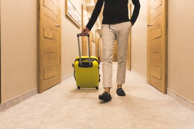 Unrecognizable man with suitcase walking through hotel hallway. 