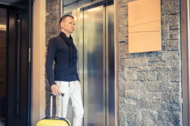 Mid adult man with travel bag standing in a hallway and waiting for the elevator. 