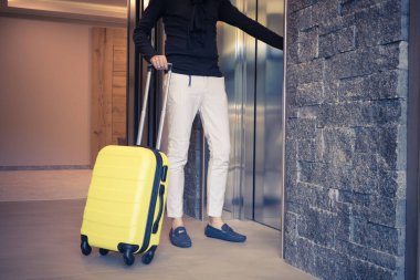 Unrecognizable man with suitcase using elevator in hotel lobby. 