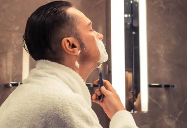 Mid adult man using razor and shaving in the bathroom. 