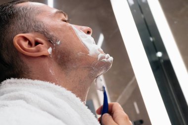 ow angle view of man shaving his face with razor in the bathroom. 