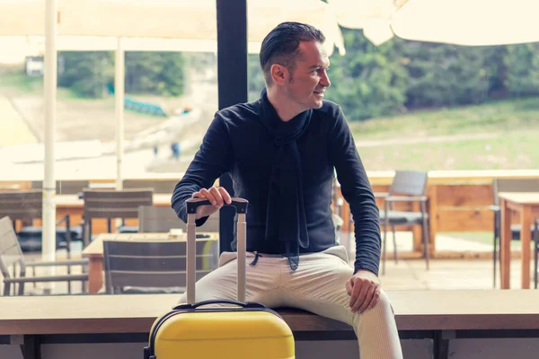 Happy mid adult man sitting with travel bag in a hallway. 