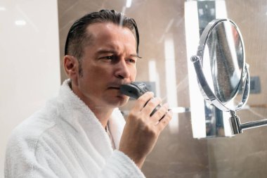 Man shaving his face with electric razor in the bathroom. 