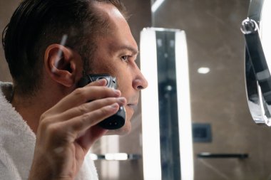 Close-up of man shaving his face with electric razor in the bathroom. 