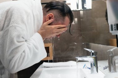 Man in bathrobe washing his face in the morning.