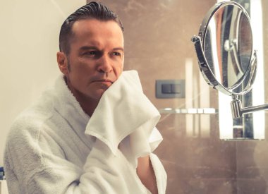 Mid adult man using towel and wiping face after shaving in the bathroom.