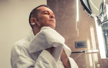 Low angle view of man wiping face with cotton towel after shaving in the bathroom.
