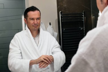 Mid adult man using hand cream while looking himself in bathroom mirror. 