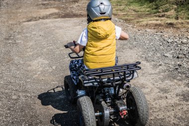 Rear view of small boy driving atv quad bike on off-road track. 