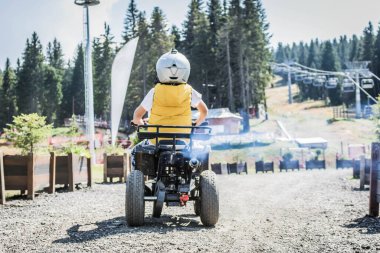 back view of child driving four wheeled atv on dirt road. 