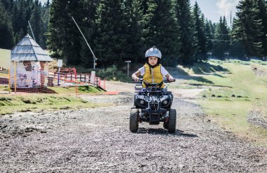 Little boy learning to drive quad bike on dirt road in nature. 