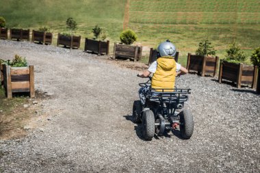 Rear view of kid learning to drive atv off-road vehicle. 