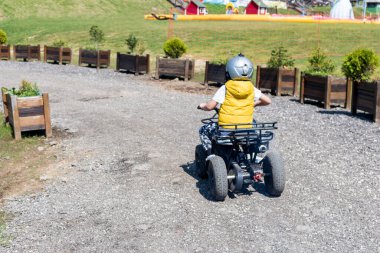 Rear view of kid driving on off road train on a quadbike. 