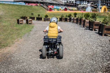 Back view of child driving quadricycle on dirt road.