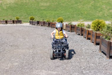 Happy boy having fun while driving quadbike on a dirt road in nature. 